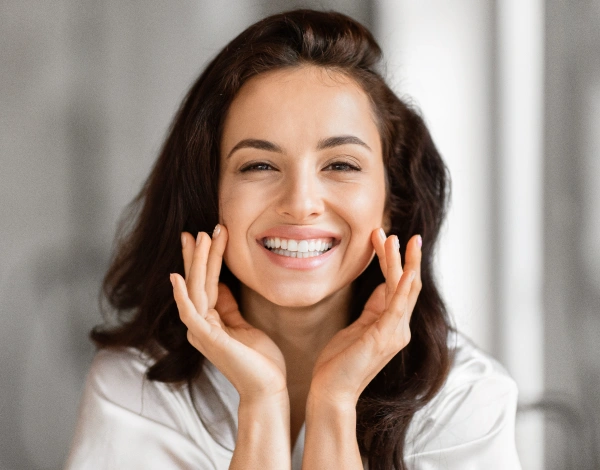 Woman smiling with hands near face in dental office setting, promoting healthy smile care.