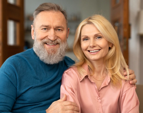 Two smiling adults posing together indoors at a dental office, wearing casual clothing.