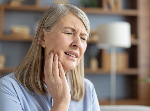 Woman experiencing tooth pain, holding her cheek, in a home interior setting.