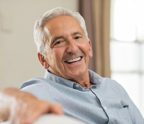 Smiling senior man in light blue shirt sitting indoors by window