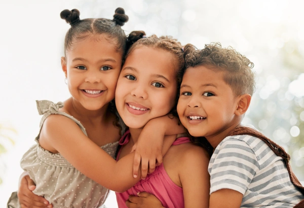 Three young girls smiling together with arms around each other in a bright, cheerful setting.