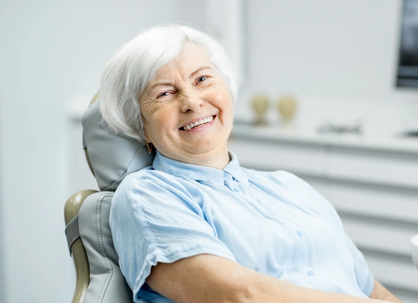 Senior woman smiling in dental chair wearing light blue bib at modern dental office.