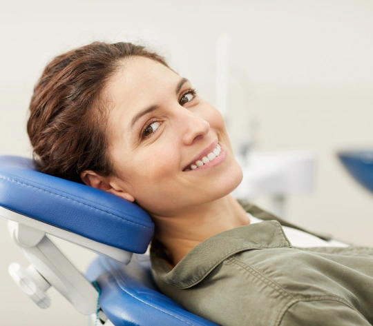 Happy woman holding blue pillow in dental office, smiling at camera.